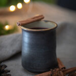 handmade ceramic mug with mulled wine with rum in a holiday setting surrounded by spices