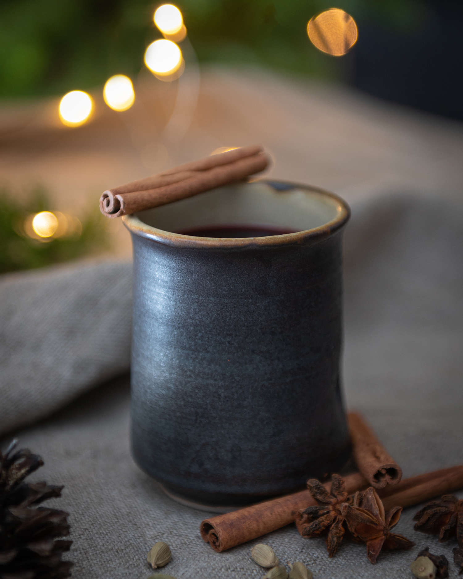 handmade ceramic mug with mulled wine with rum in a holiday setting surrounded by spices